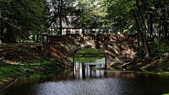 Eine Brücke aus Stein über einem Gewässer, das beidseitig von Wald umgeben ist.