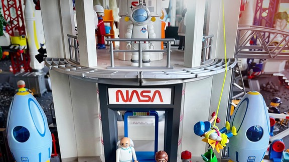 Playmobil-Figuren stehen vor einer nachgebauten NASA-Zentrale. Auf dem Balkon steht ein Astronaut. 