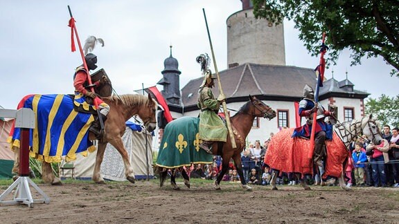 Mehrere Ritter in Rüstungen sitzen auf prachtvoll geschmückten Pferden