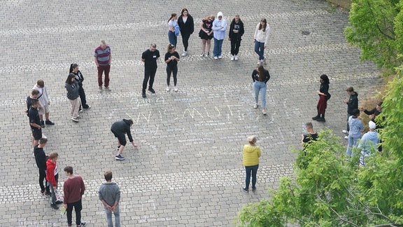 Mehrere Menschen stehen in einem Hof um eine in Mindmap zum Thema Wismut, die mit Kreide auf den Boden gemalt wurde. 