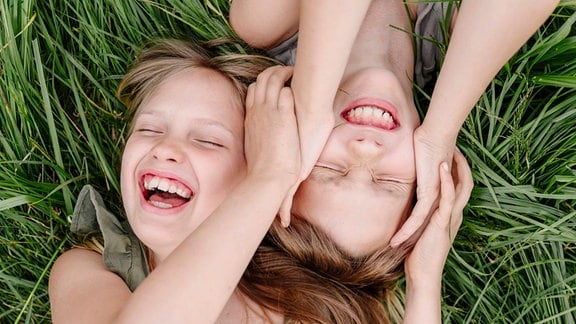 Stimmungsbild zum Thema Kinder im Sommer: Zwei Kinder liegen auf einer Wiese und lachen.