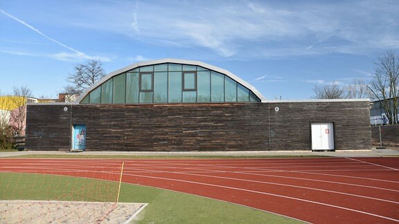 Eine Sporthalle in Magdeburg: ein flacher Bau mit dunkelbrauner Verkleidung, darüber eine Kuppel aus Glas