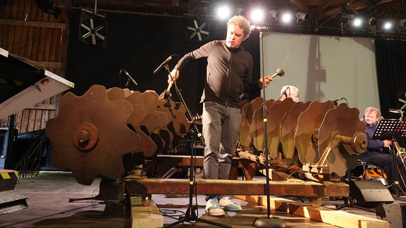 Musiker Gareth Lubbe probt vor Beginn der Stelzenfestspiele in der Festscheune an einer Scheibenegge. 