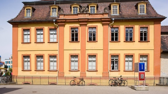 Eine Frontansicht des Wittumspalais in Weimar bei gutem Wetter ist zu sehen, das Gebäude ist in gelb und orange gehalten