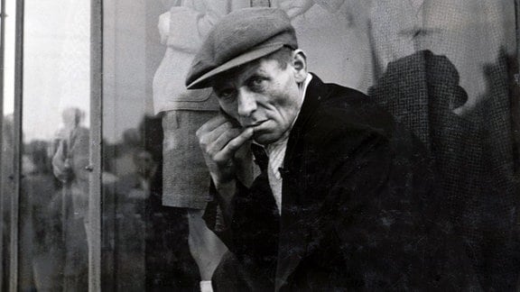 Schwarz-Weiß-Foto eines Mannes mit Mütze vor einem Schaufenster.   