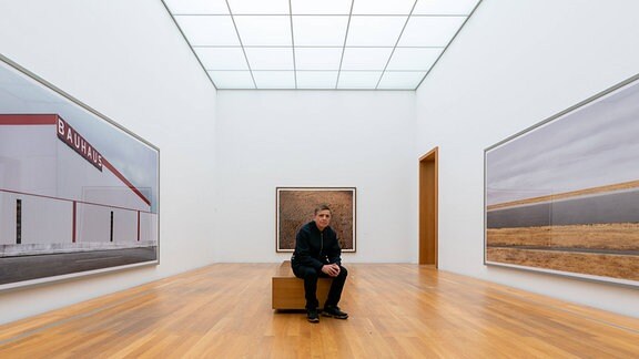 Der Fotograf Andreas Gursky sitzt vor seinen Werken l-r Bauhaus 2020, Ohne Titel III 1996 und Rhein III 2018 im Museum der bildenden Künste MdbK in Leipzig. 