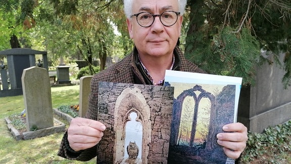 Mann steht auf Friedhof und hält Bilder in der Hand.