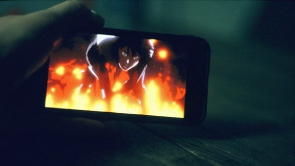 Auf einem Smartphonebildschirm leuchtet ein Bild auf, das eine Anime-Figur in Flammen zeigt.