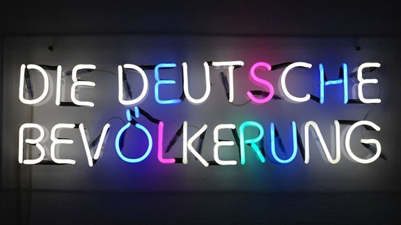 Bund erleuchtete Buchstaben formen sich zum Schriftzug "Die Deutsche Bevölkerung", Lichtinstallation von Silke Wagner