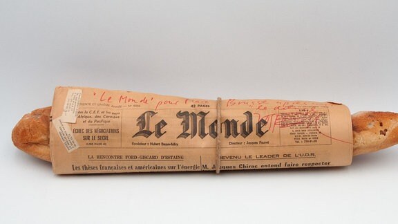 Kunstwerk von Wolf Vostell, zu sehen ist ein in eine Zeitung eingerolltes Baguette, auf der steht "Le Monde"
