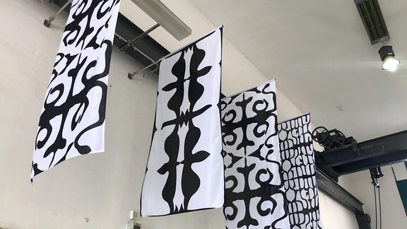 4 weiße Banner mit schwarzen Mustern hängen von der Decke.