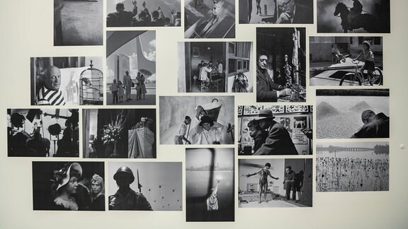 Zu sehen ist eine Collage aus verschiedenen schwarz-weiß Fotografien des Fotografen René Burri an einer cremefarbenen Wand.