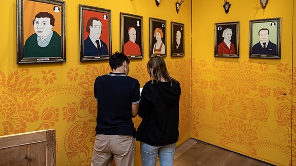 Zwei Personen lösen ein Rätsel vor einer Bildergalerie mit Porträts u.a. von Martin Luther