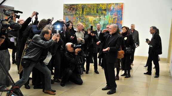 Ein als der Maler Gerhard Richter bekannter Mann steht in einer Kunstgalerie vor einer Gruppe von Journalistinnen und Fotografen