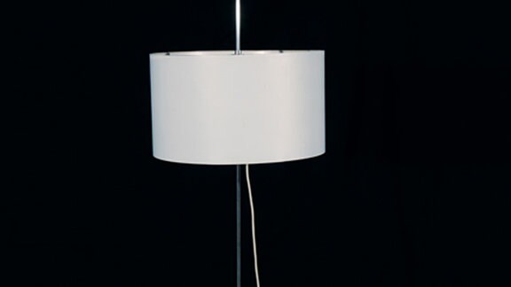 Stehlampe mit weißem Schirm vor einer schwarzen Wand