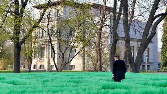 Ein Gebäude, hinter Bäumen versteht, davor umgestülpte grüne Besen - ein Kunstwerk von Olaf Nicolai.