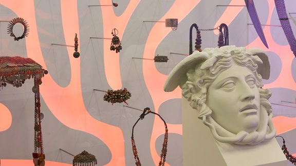 Blick in eine Ausstellung, vorn die Skulptur eines Frauenkopfs, im Hintergrund hängen verschiedene Ausstellungsstücke an der Wand