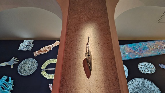 In einer Ausstellung hängt ein beleuchteter Stein an einer Säule.