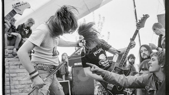 Heavy Metal Konzert: Headbanging auf der Bühne, gefeiert von jungen Männern im Publikum, Schwarz-Weiß-Foto zu sehen in der Ausstellung: "Heavy Metal in der DDR" in der Berliner Kulturbrauerei
