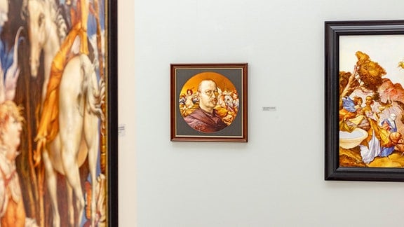 Blick in eine Ausstellung mit Gemälden, darunter das Selbstporträt eines Mannes