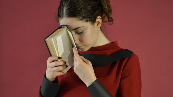 Eine junge Frau hält ihren Kopf mit geschlossenen Augen an ein Buch