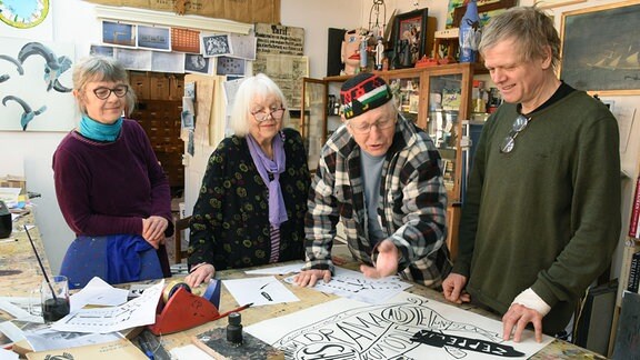 Vier Menschen stehen an einem Tisch mit Zeichnungen von Entwürfen.