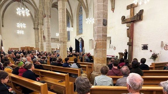 In einer Kirche sitzen viele Menschen, eine Frau spricht am Rednerpult in ein Mikrofon.