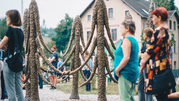 Menschen stehen um eine Bronze-Skulptur in Form von Zweigen herum.