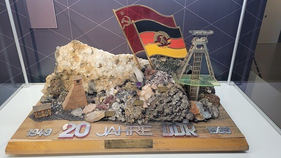 Eine Skulptur zum Gedenken an "20 Jahre DDR" beinhaltet eine DDR- und eine Sowjetische Fahne, sowie einen Förderturm neben großen Steinen.