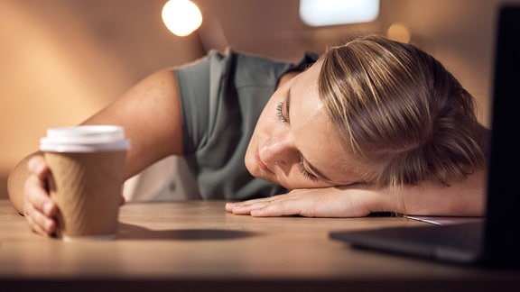 Eine Frau liegt mit dem Kopf auf dem Schreibtisch