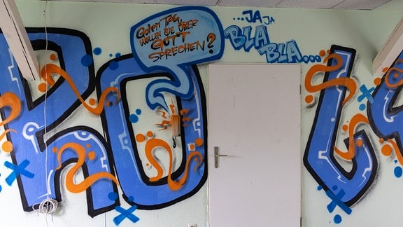 Blaue Schrift auf weißer Wand - Graffiti-Schriftzug: "Möchten Sie über Gott sprechen?"