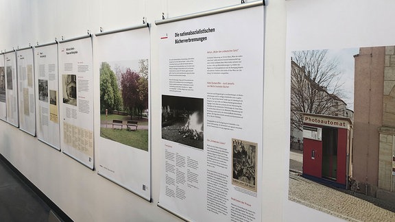 Vor einer weißen Wand hängen mehrere Tafeln mir Texten und Fotografien