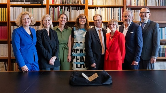 Menschen stehen vor einer Regalwand mit Büchern