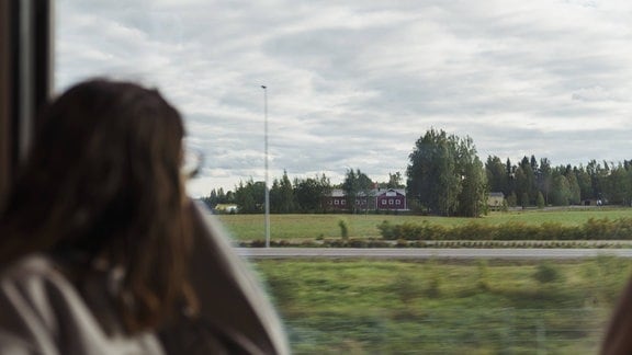 Eine junge Frau schaut aus dem Fenster eines fahrenden Zuges.
