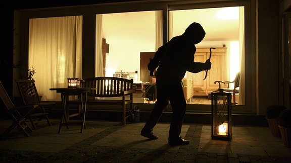 Symbolbild Einbruch, Einbrecher will in ein Haus eindringen, schleicht sich auf der Terrasse an. 