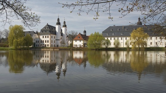 Schloss Blankenhain, eine Anlage aus mehreren Gebäuden mit weißer Fassade, umgeben von einem See und Bäumen