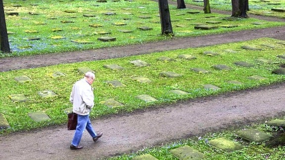 Ein Mann spaziert an Grabkissen auf dem Herrnhuter Friedhof Neudietendorf entlang