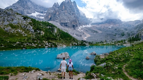 Ein Paar steht vor dem  milchig blauen See Lago di Sorapis oder dem Sorapis-See in den italienischen Dolomiten. 