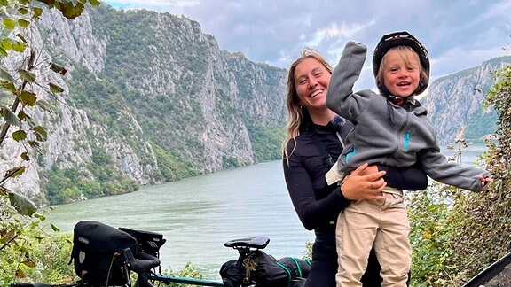 Frau und Kind mit einem Fahrrad vor einem Bergsee.