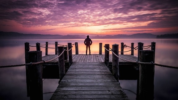 Ein Mann steht bei Sonnenuntergang auf einem Steg