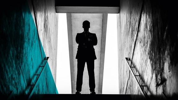 Silhouette eines Mannes, der am oberen Ende eines Treppenaufgangs über dem Betrachter steht.