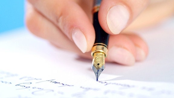 eine Hand mit Federhalter beim Schreiben auf ein Blatt Papier