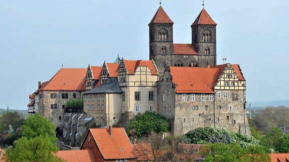 Die Stiftskirche aus Stein in Quedlinburg steht auf einem Hügel vor blauem Himmel, die Dächer sind rot gehalten