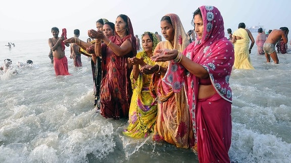 Hindu Frauen stehen mit ihren Kleidern bis zu den Knien im Wasser.