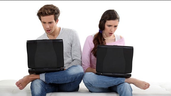 Ein Paar sitzt mit Laptop-Computern auf einem Bett.