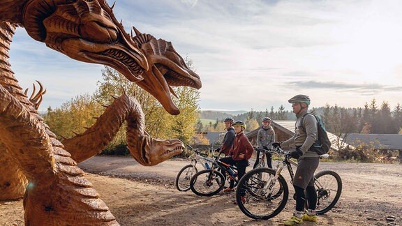 Radfahrer vor einer Drachenfigur aus Holz