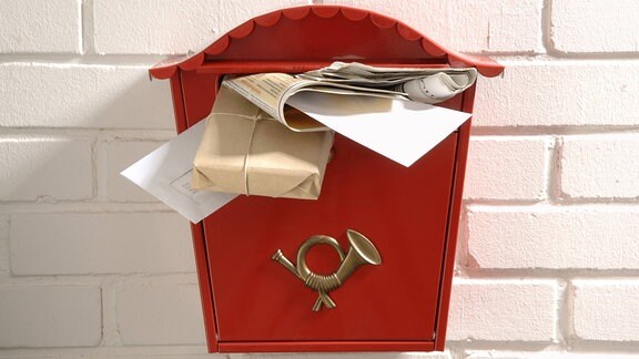 Roter Briefkasten überladen mit Briefen und Päckchen