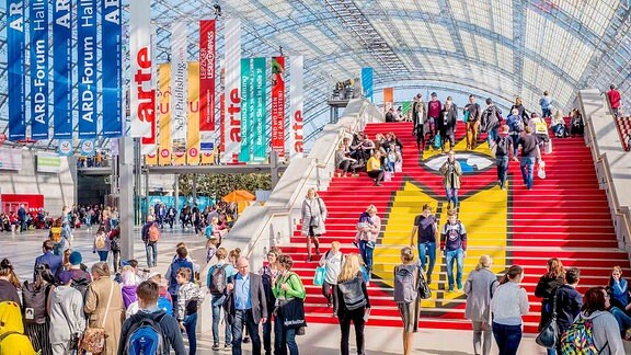 Impression von 2019: Mehrere Menschen gehen auf eine Treppe zu, auf der das Logo der Leipziger Buchmesse zu ist.