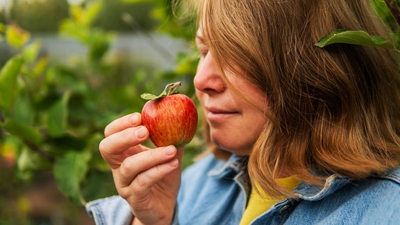 Eine Frau riecht an einem frisch geernteten Apfel.