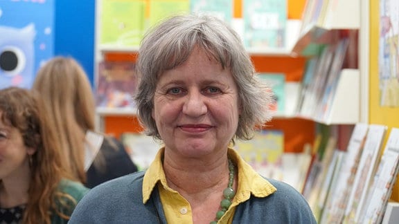 Monika Osberghaus, eine Frau vor Büchern, vor denen Menschen sind.